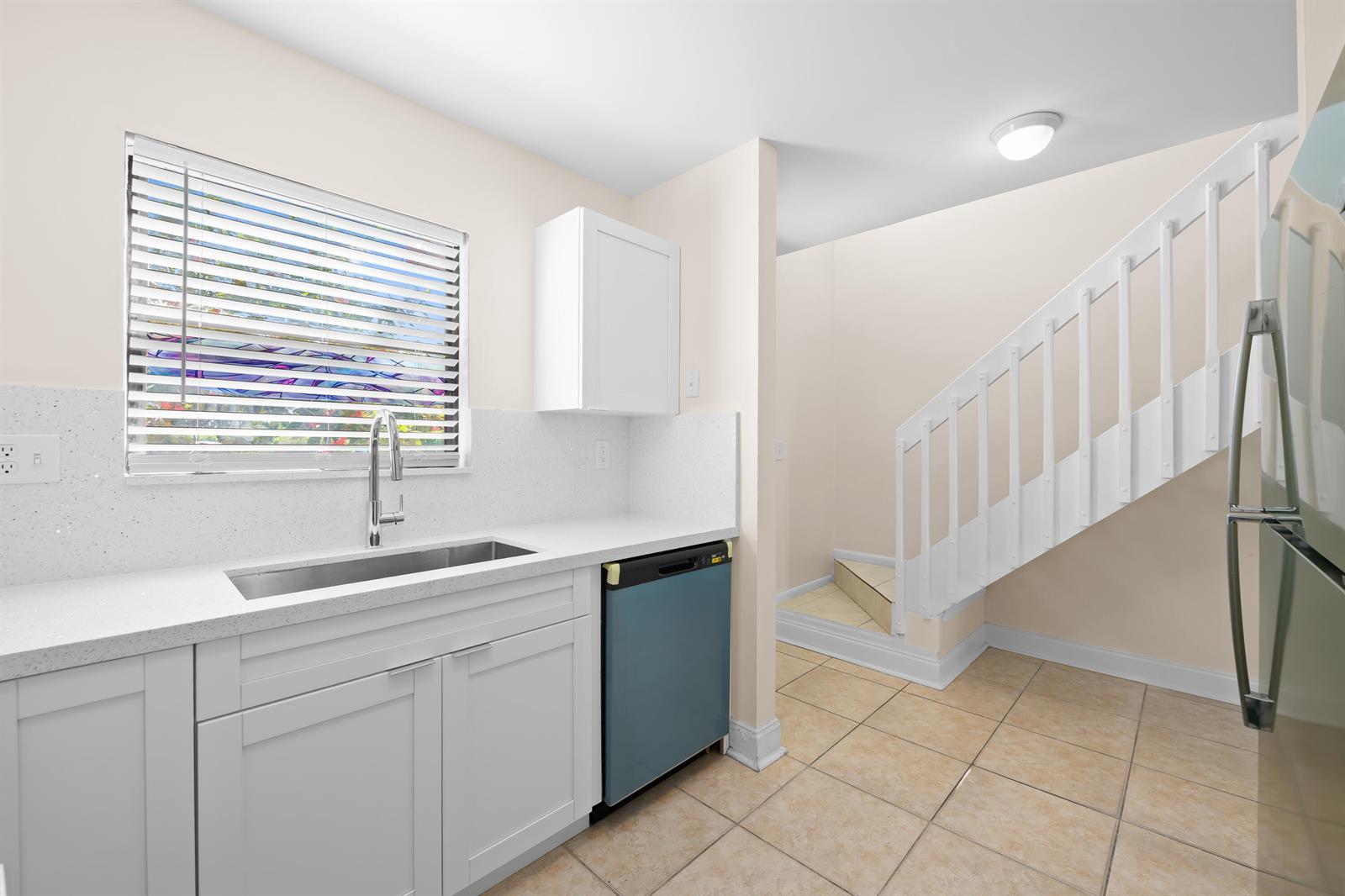 A kitchen features white cabinets, a quartz countertop, a stainless steel sink, and a staircase — 3281 E Golf Boulevard # 4, Pompano Beach FL 33064, POMPANO BEACH, FL