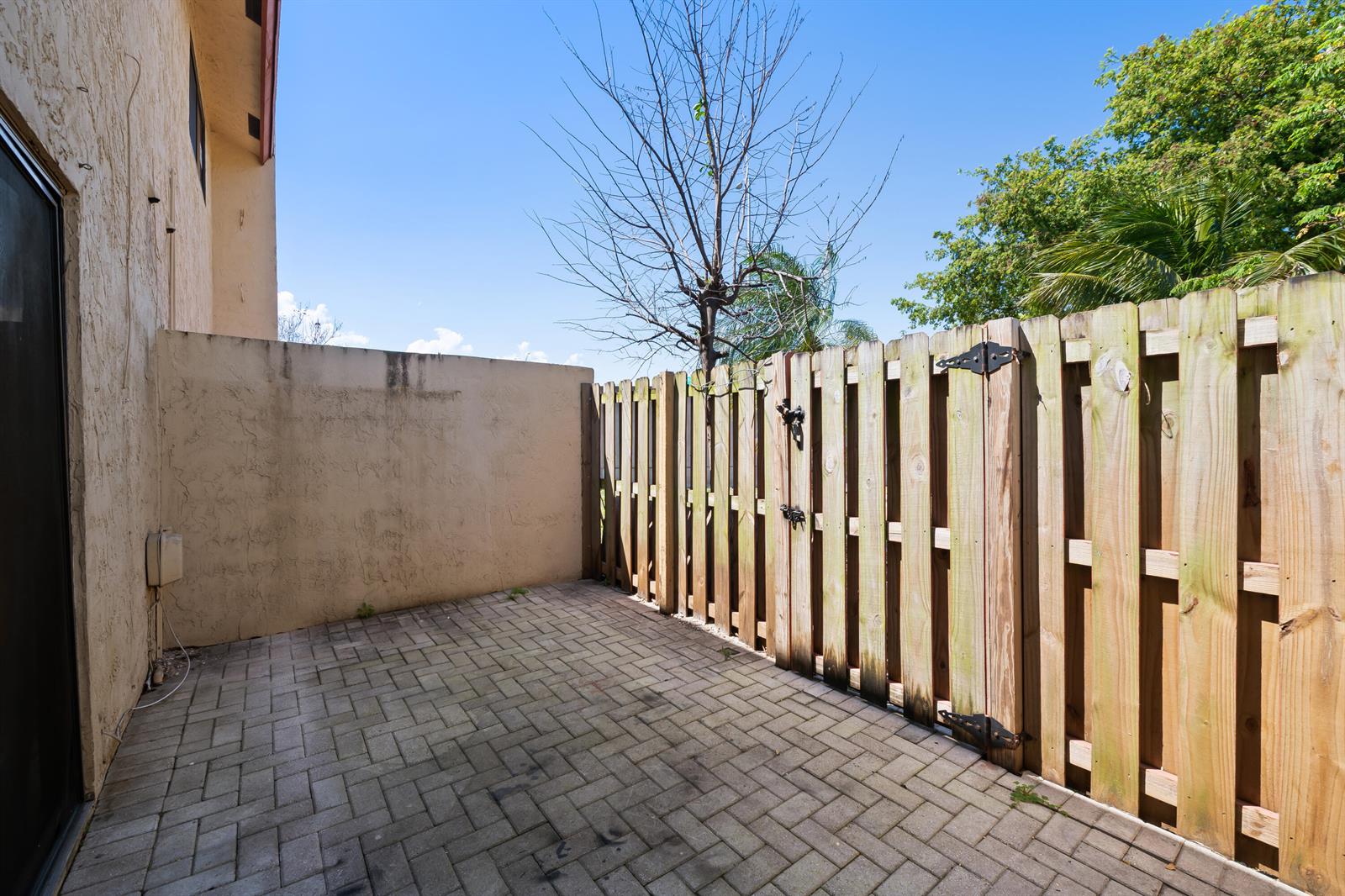 A paved patio area features a stucco wall and a wooden privacy fence — 3281 E Golf Boulevard # 4, Pompano Beach FL 33064, POMPANO BEACH, FL