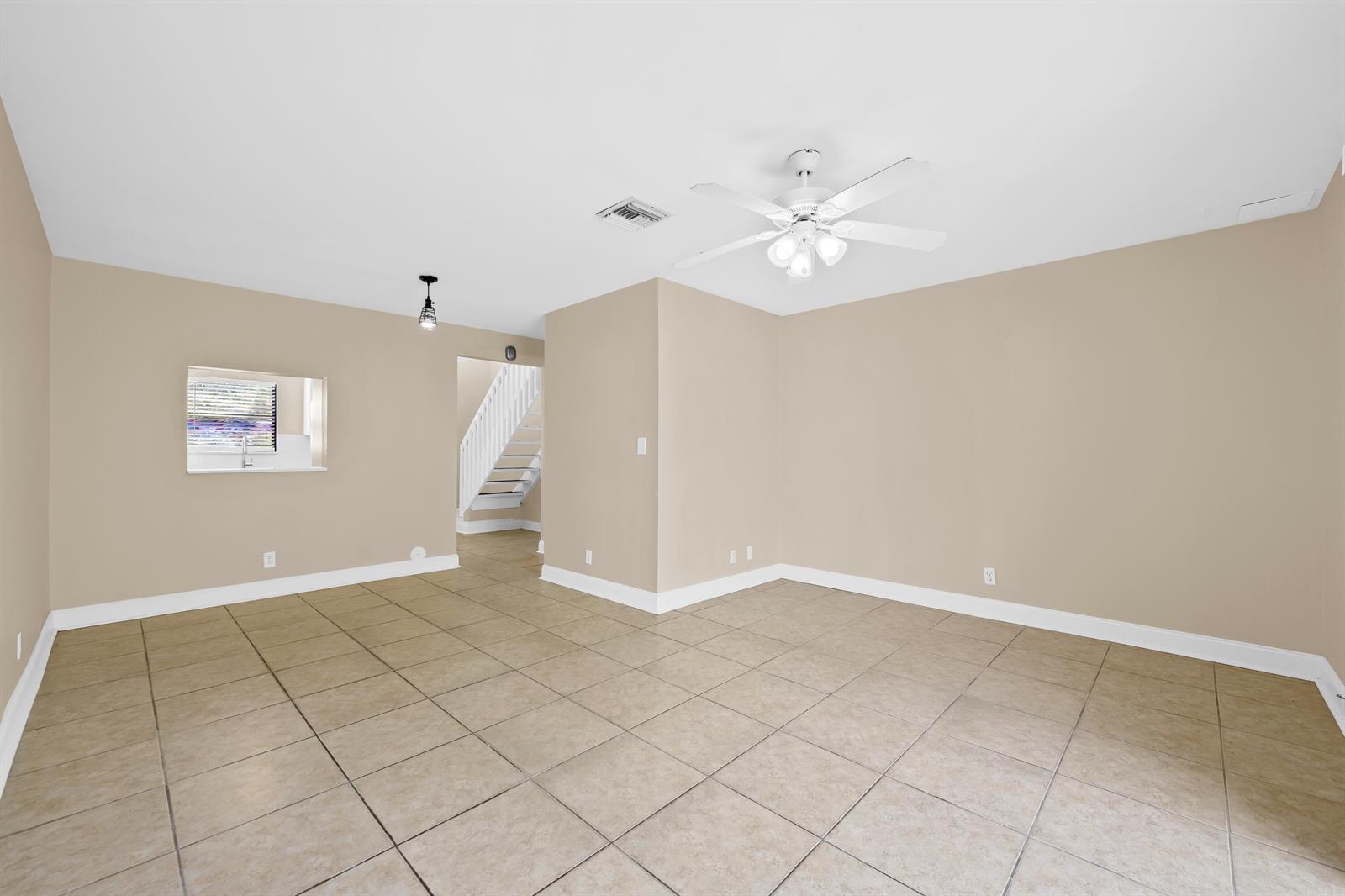 An empty room with beige walls, tile flooring, a ceiling fan, and a staircase visible — 3281 E Golf Boulevard # 4, Pompano Beach FL 33064, POMPANO BEACH, FL