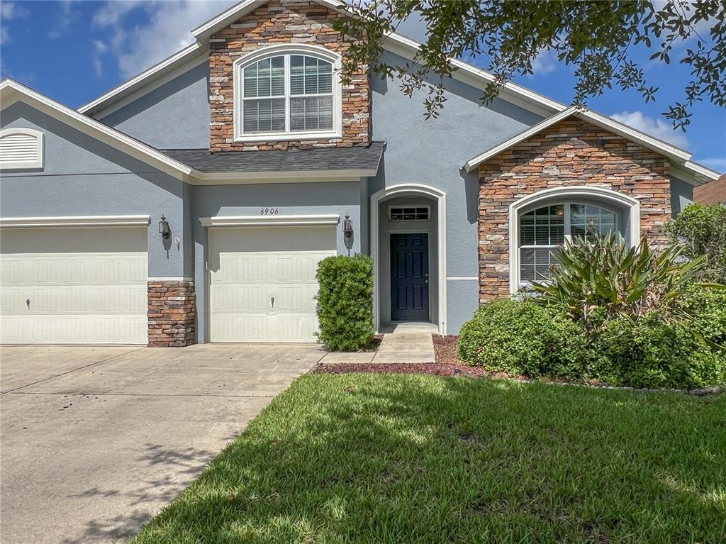 A two-story house features a blue stucco exterior, stone accents, and a two-car garage — 6906 BOULDER RUN LOOP, WESLEY CHAPEL, FL