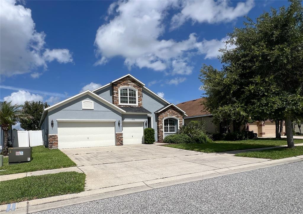 A two-story suburban house with a three-car garage, stone accents, and a concrete driveway — 6906 BOULDER RUN LOOP, WESLEY CHAPEL, FL