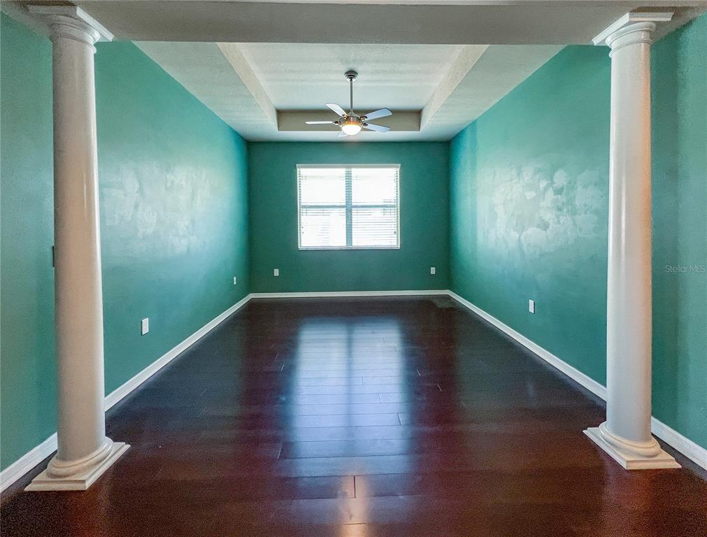 A room with teal walls, dark wood flooring, a tray ceiling, and two white columns — 6906 BOULDER RUN LOOP, WESLEY CHAPEL, FL