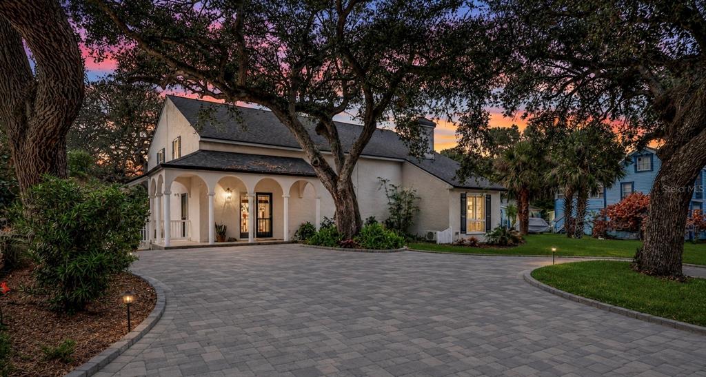 A two-story house with a paved driveway, arched porch, and large trees at sunset — 111 ESTHER STREET, NEW SMYRNA BEACH, FL