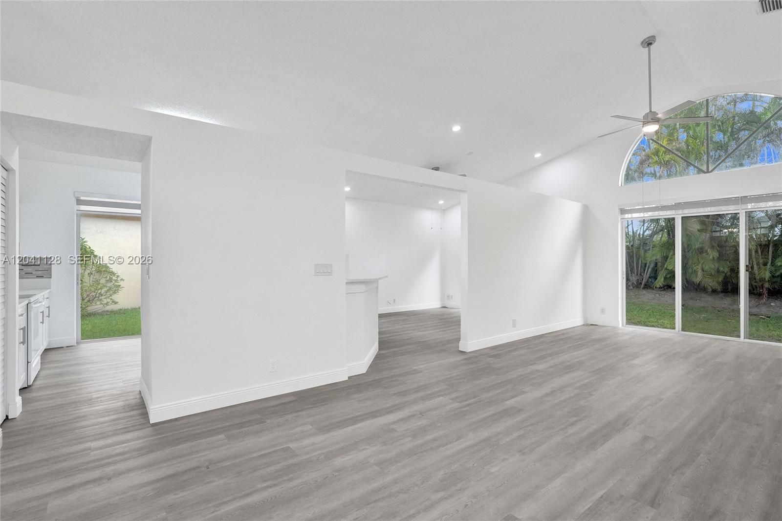 An open-concept living area features vaulted ceilings, gray wood-look flooring, and large sliding glass doors — 6931 NW 34th St # 6931, Margate FL 33063, MARGATE, FL