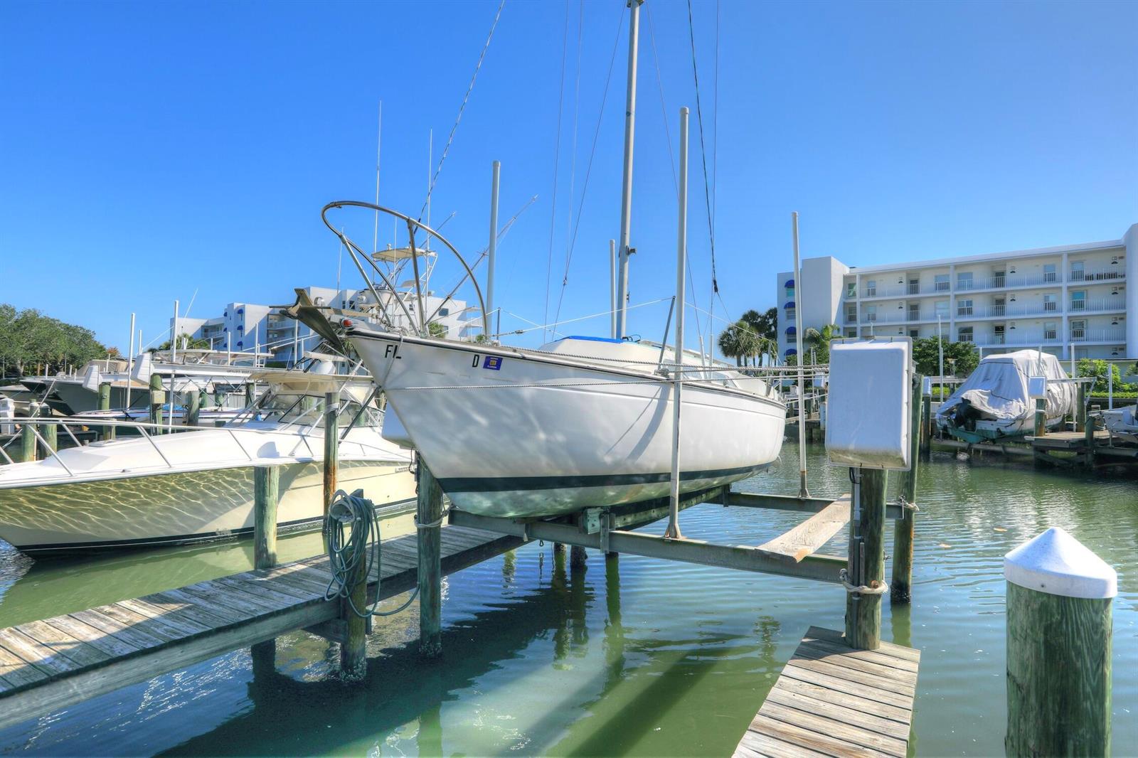 A white sailboat sits on a boat lift at a marina near a residential building — SEBASTIAN, FL