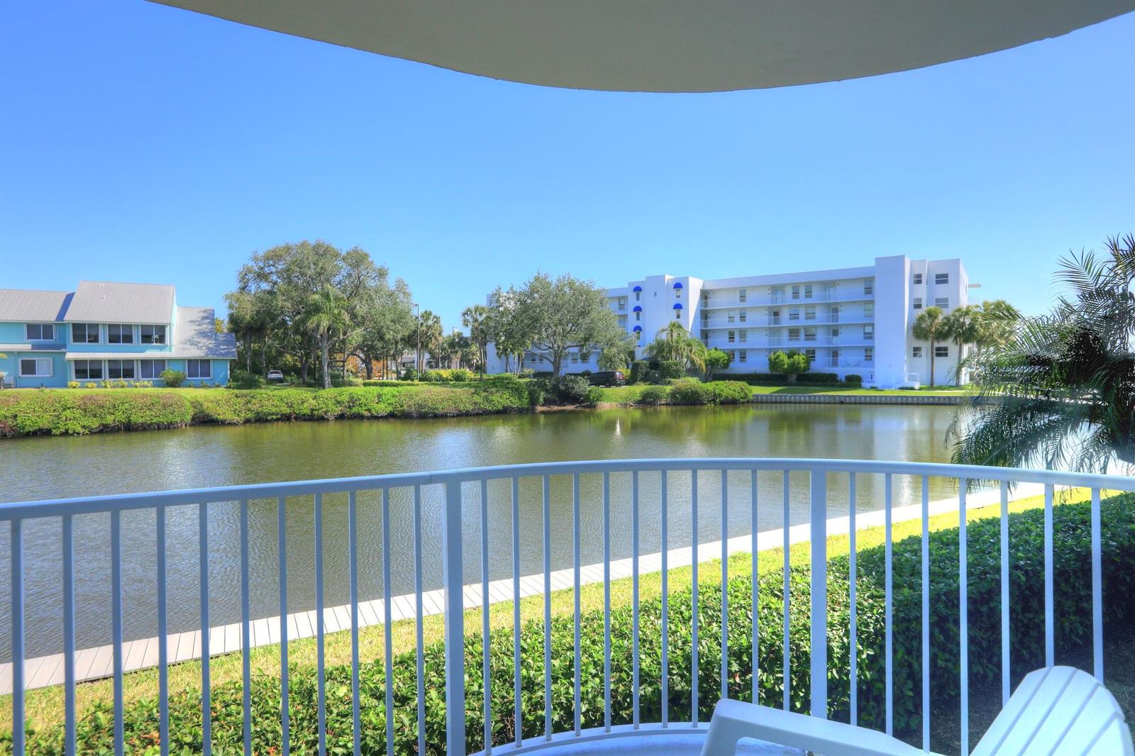 A balcony view overlooking a pond, green landscaping, and multi-story residential buildings under a sky — SEBASTIAN, FL