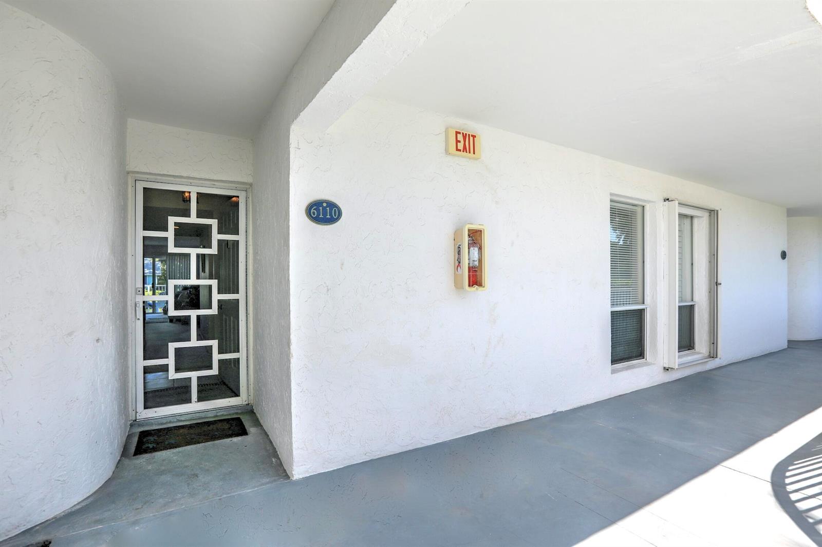 A white exterior building entrance features a decorative glass door, a fire extinguisher, and windows — SEBASTIAN, FL