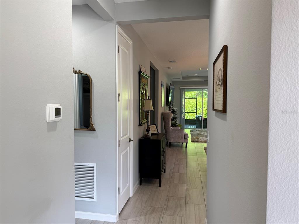 A hallway with light gray walls and tile flooring leads toward a sunlit living area — 173 OLD MOSS CIRCLE, DELAND, FL