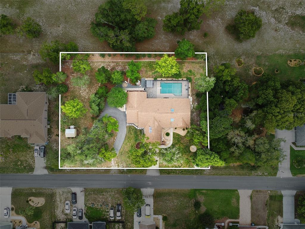 An aerial view shows a house with a swimming pool on a wooded residential lot — 5105 KEYSVILLE AVENUE, SPRING HILL, FL