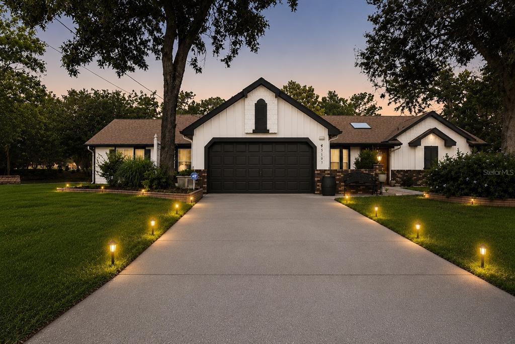 A single-story house with a black garage door, white siding, and a lit concrete driveway — 5105 KEYSVILLE AVENUE, SPRING HILL, FL