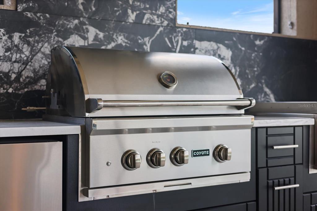 A stainless steel Coyote outdoor grill is built into a dark cabinet with marble backsplash — 13730 HEARTWOOD WAY, PARRISH, FL