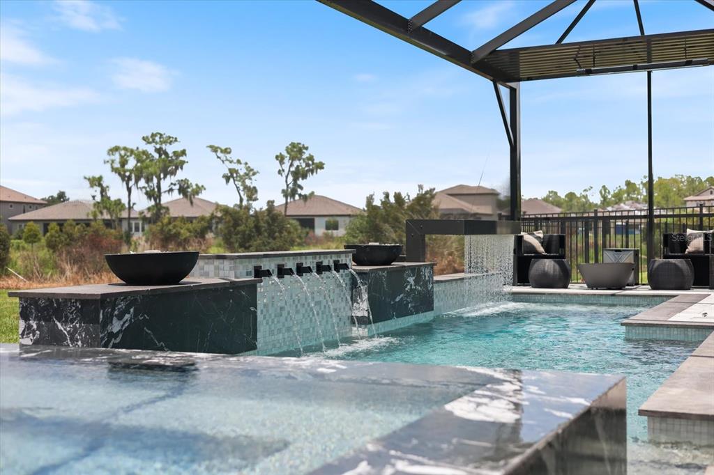 A swimming pool with a water feature and spa sits under a screened-in patio enclosure — 13730 HEARTWOOD WAY, PARRISH, FL