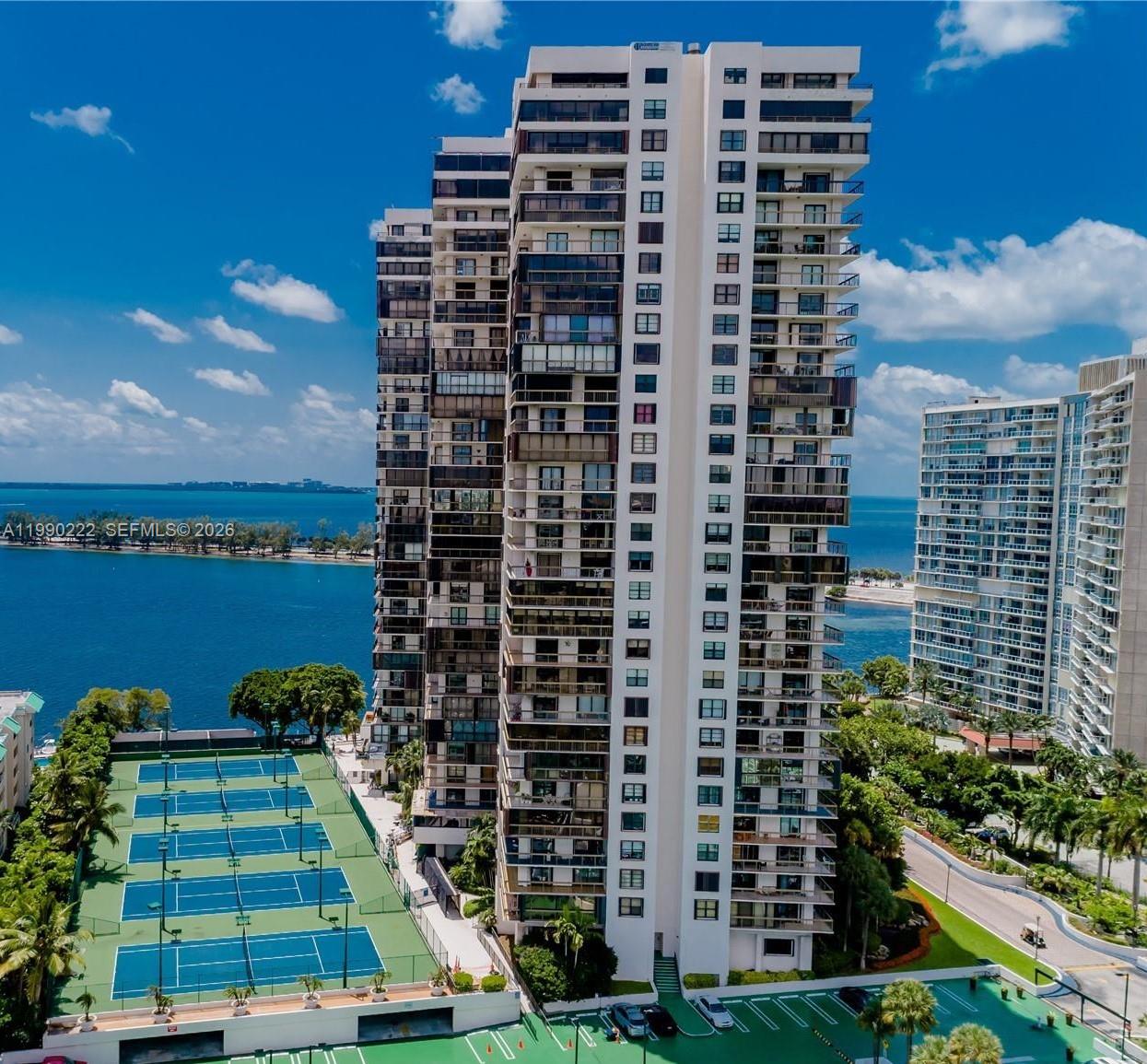 An aerial view shows a tall residential high-rise building next to tennis courts and water — 2333 Brickell Ave # 2607, Miami FL 33129, MIAMI, FL