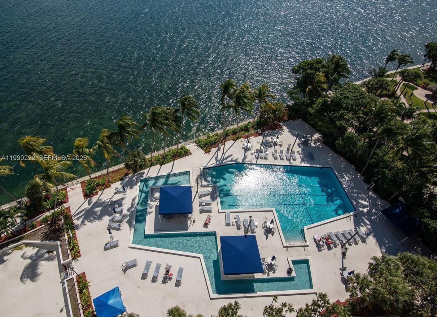 An aerial view shows a swimming pool with lounge chairs and umbrellas beside a bay — 2333 Brickell Ave # 2607, Miami FL 33129, MIAMI, FL