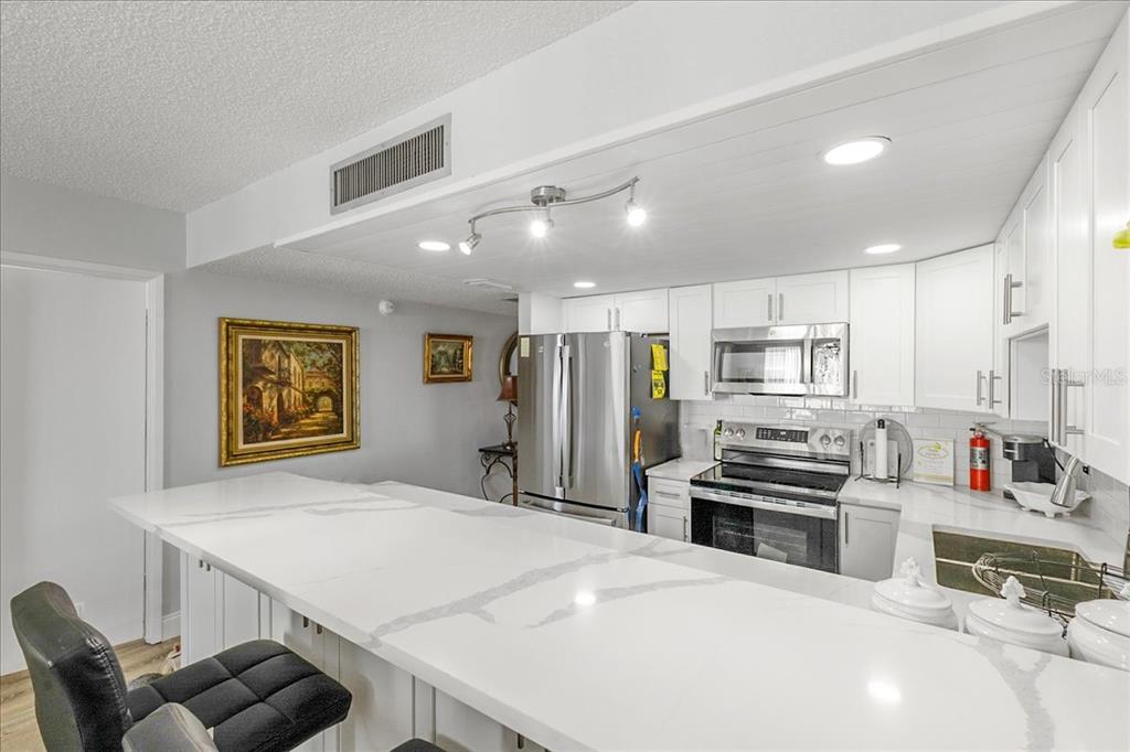 A kitchen features white cabinets, stainless steel appliances, and a large white quartz breakfast bar — 2947 S ATLANTIC AVENUE UNIT 506, DAYTONA BEACH, FL