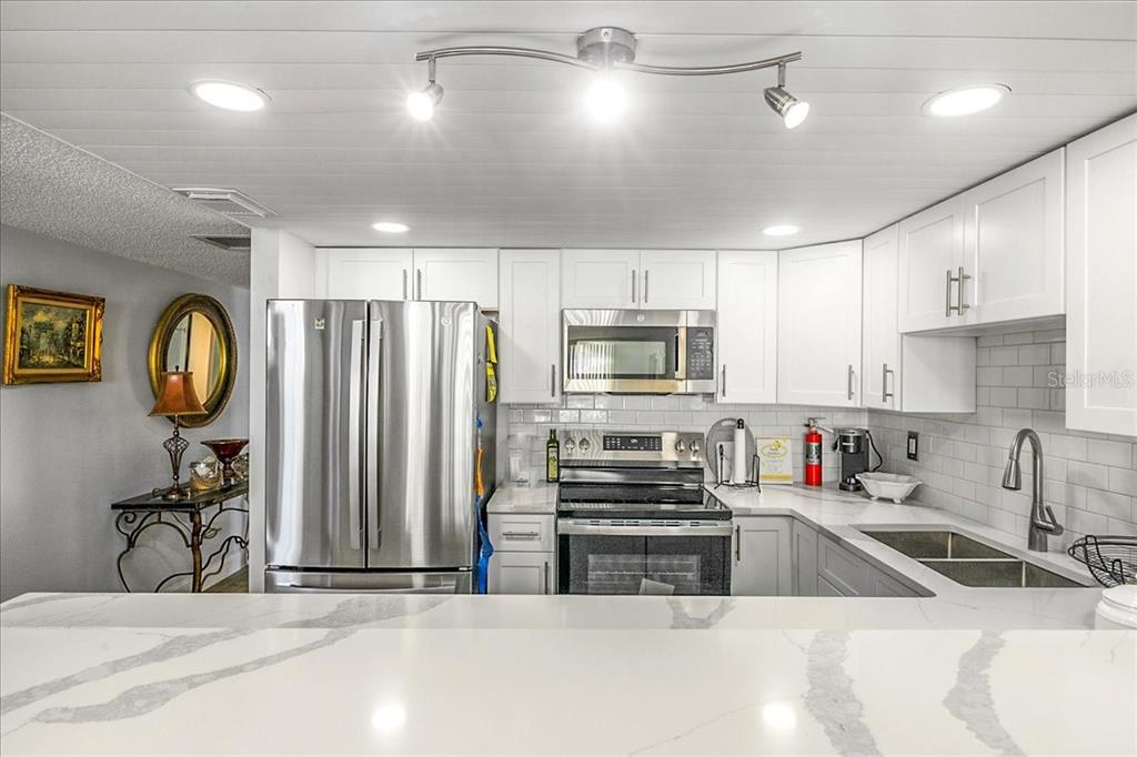 A kitchen features white cabinets, stainless steel appliances, and a white marble-look countertop — 2947 S ATLANTIC AVENUE UNIT 506, DAYTONA BEACH, FL