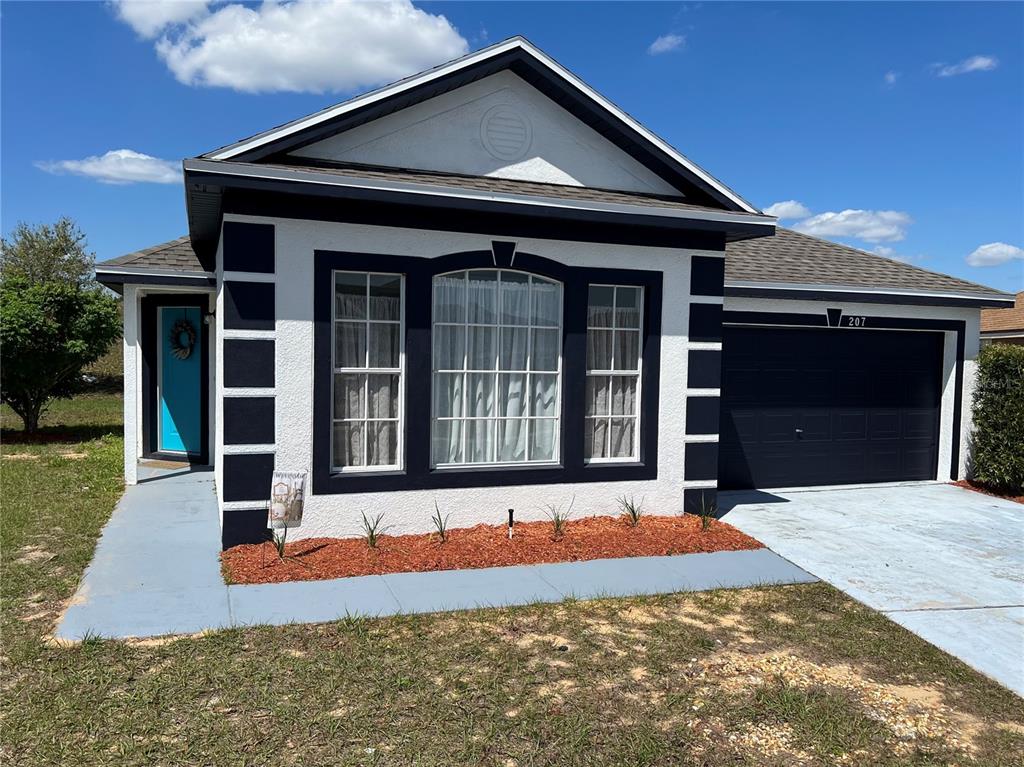 A single-story house with white stucco walls, dark trim, a front bay window, and garage — 207 HIGH RIDGE DRIVE, DAVENPORT, FL