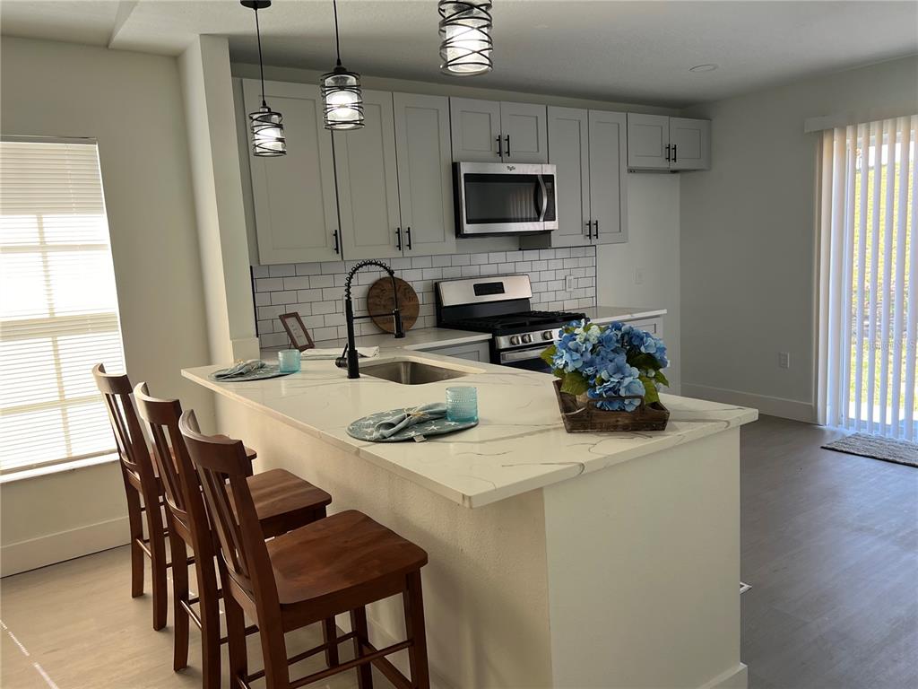 A kitchen features light gray cabinets, a white quartz island with bar seating, and subway tile — 207 HIGH RIDGE DRIVE, DAVENPORT, FL