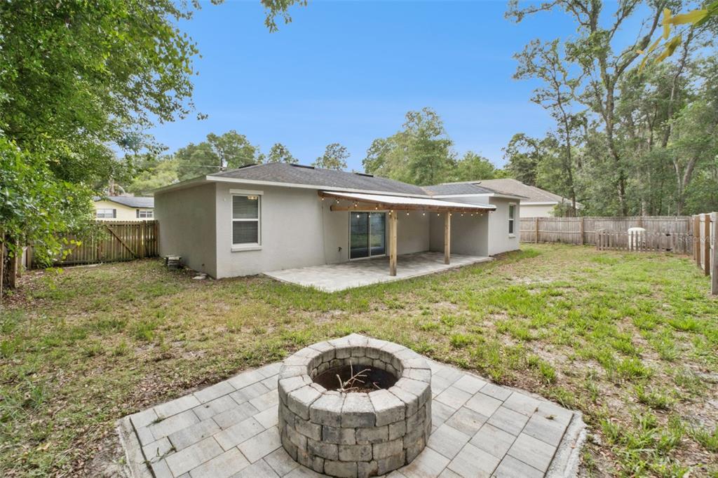 A backyard features a stone fire pit, a concrete patio, and a covered wooden porch — 1221 3RD STREET, ORANGE CITY, FL