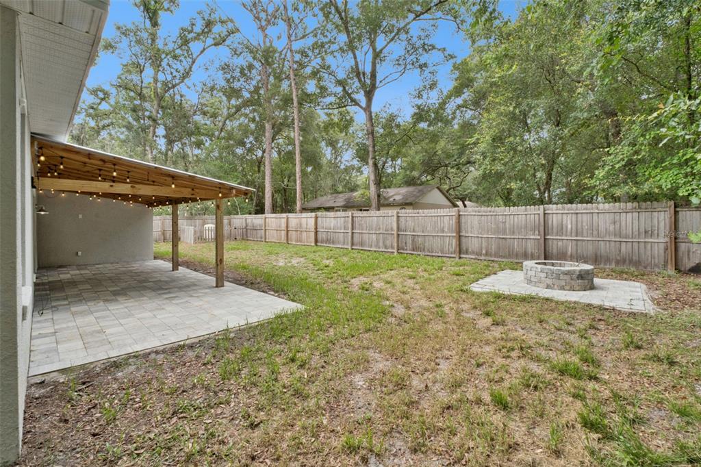 A backyard features a covered patio with string lights, a fire pit, and a wooden fence — 1221 3RD STREET, ORANGE CITY, FL