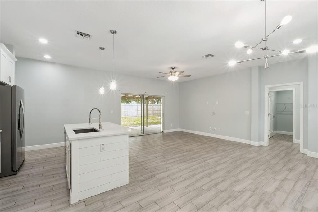 A kitchen island with a sink sits in an open-concept room with light wood-look flooring — 1221 3RD STREET, ORANGE CITY, FL