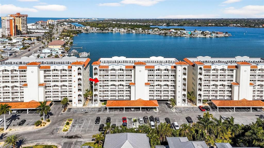 An aerial view shows a multi-story apartment building with a red-tiled roof near water — 17717 GULF BOULEVARD UNIT 401, REDINGTON SHORES, FL