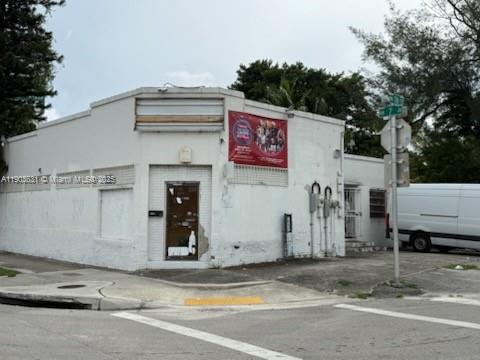 A white, single-story commercial building sits on a corner lot with a street sign nearby — 11628 NW 7th Ave, Miami FL 33168, MIAMI, FL