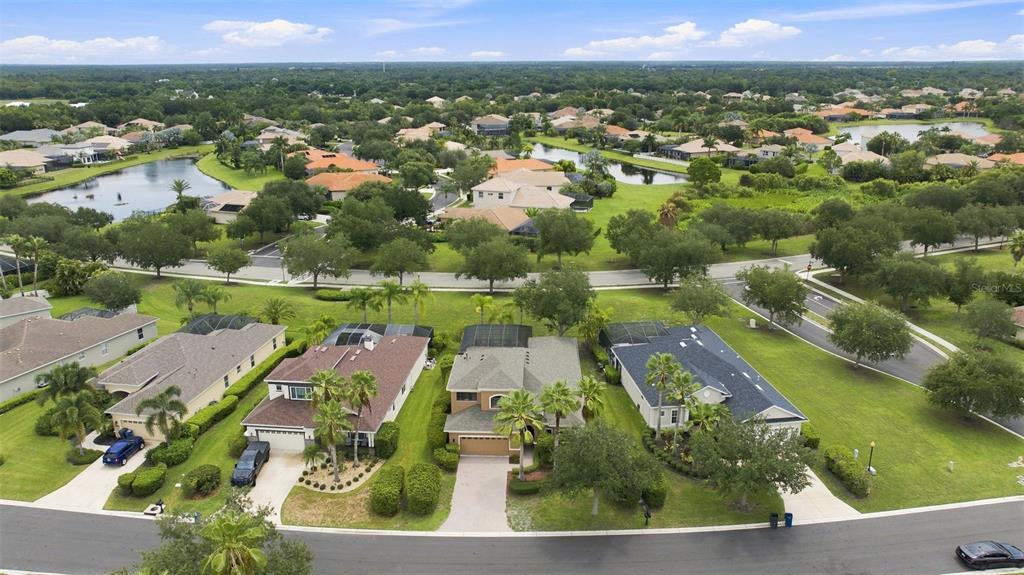 An aerial view shows suburban houses with swimming pool enclosures and lawns near a lake — 235 DAHLIA COURT, BRADENTON, FL