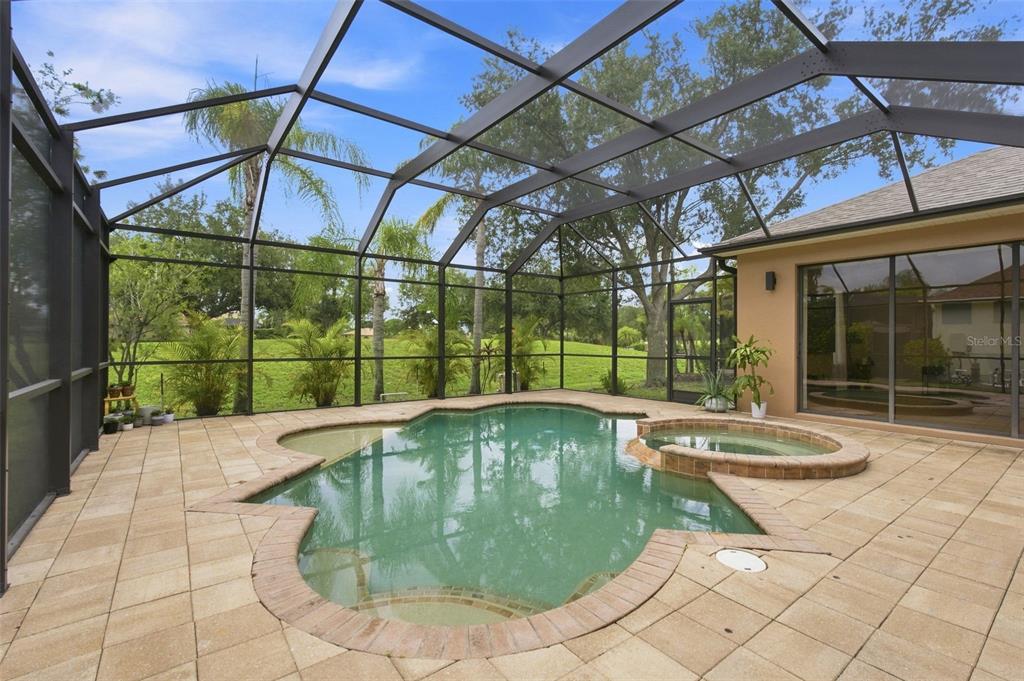 A screened-in patio features a custom-shaped swimming pool and an attached spa on a deck — 235 DAHLIA COURT, BRADENTON, FL