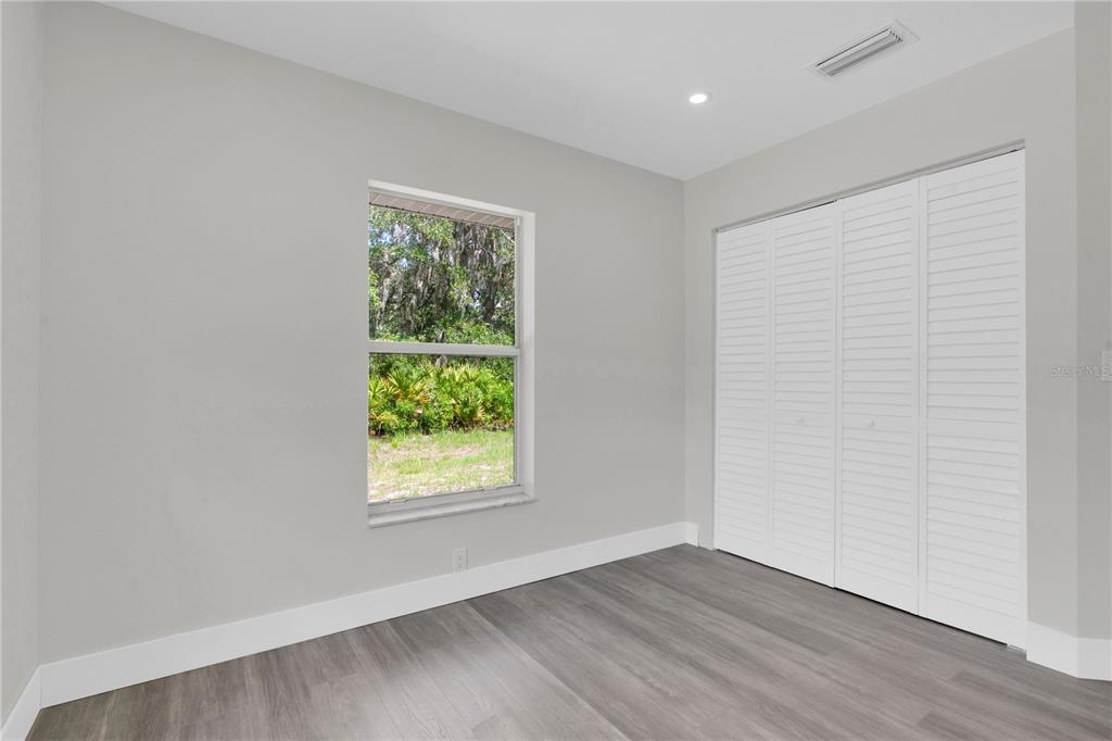 A bedroom features light gray walls, wood-look flooring, a single window, and white louvered closet doors — 3450 PARK AVENUE, INDIAN LAKE ESTATES, FL