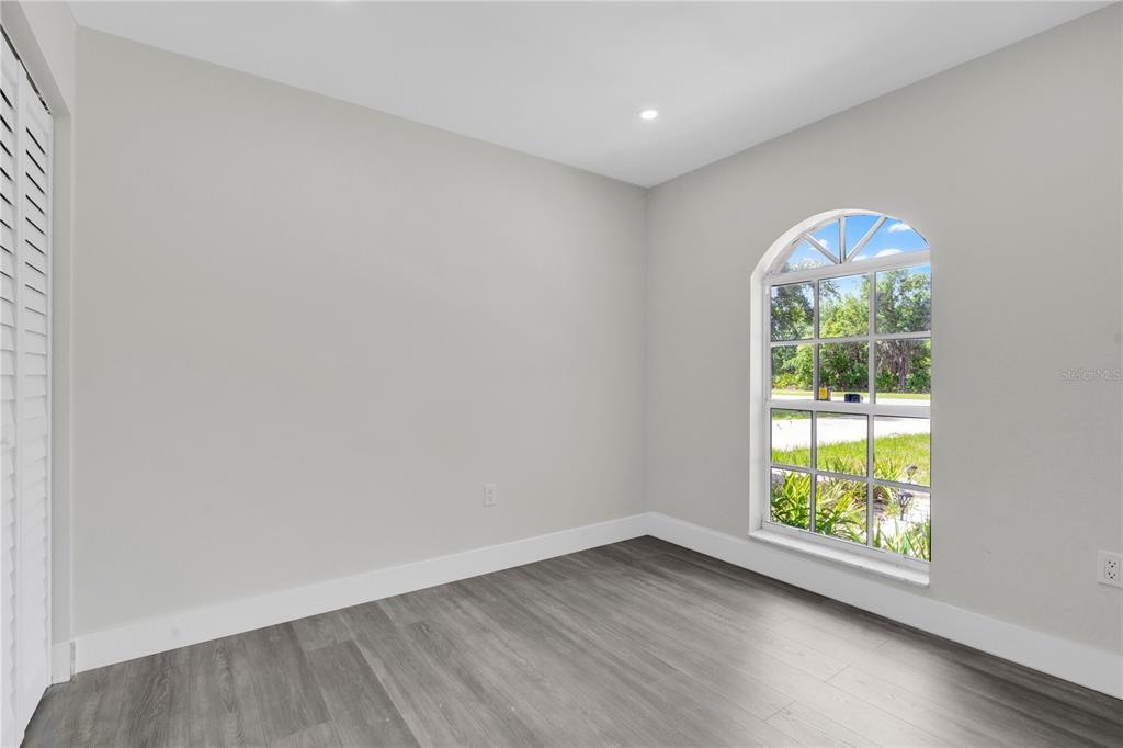 An empty room with gray wood-look flooring, white walls, and an arched window — 3450 PARK AVENUE, INDIAN LAKE ESTATES, FL