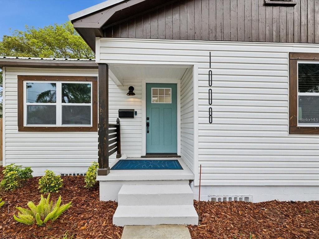 A white house exterior features a teal front door, dark wood trim, and vertical numbers — 1008 E NORFOLK STREET, TAMPA, FL