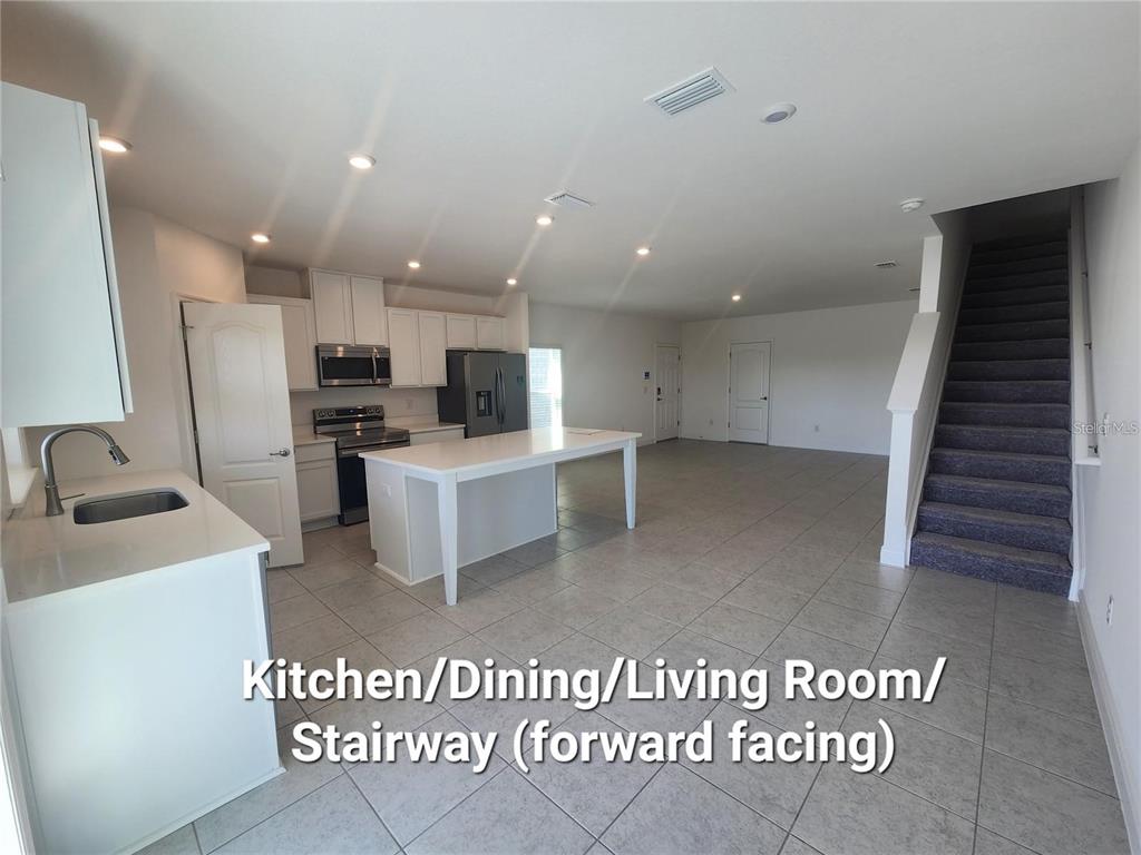 An open-concept kitchen and living area features white cabinetry, a central island, and carpeted stairs — 32118 POND APPLE BEND, SAN ANTONIO, FL