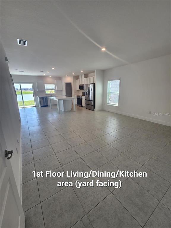 An open-concept kitchen and living area features light tile flooring and a sliding glass door — 32118 POND APPLE BEND, SAN ANTONIO, FL