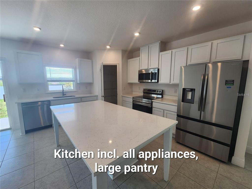 A kitchen features white cabinets, stainless steel appliances, a large island, and tile flooring — 32118 POND APPLE BEND, SAN ANTONIO, FL