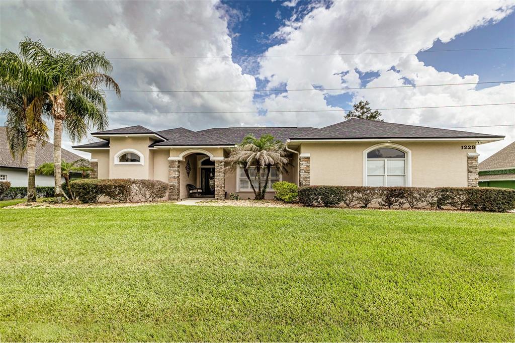 A single-story house with a beige stucco exterior, stone accents, and a large front lawn — 1229 LAKE DEESON WOODS LANE, LAKELAND, FL