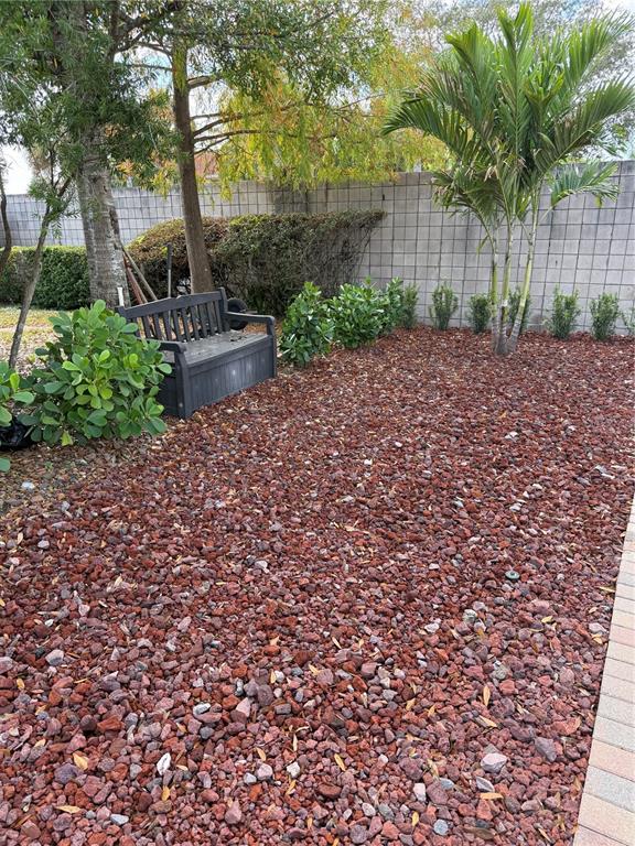 A backyard features a dark bench, red gravel ground cover, and various shrubs and trees — 6731 AMANDA VISTA CIRCLE, LAND O LAKES, FL