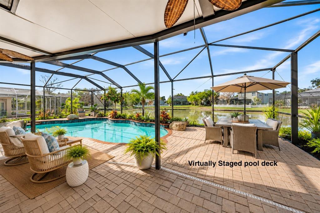 A screened-in pool deck features patio furniture, potted plants, and a view of a lake — 5128 HARTWELL LOOP, LAND O LAKES, FL