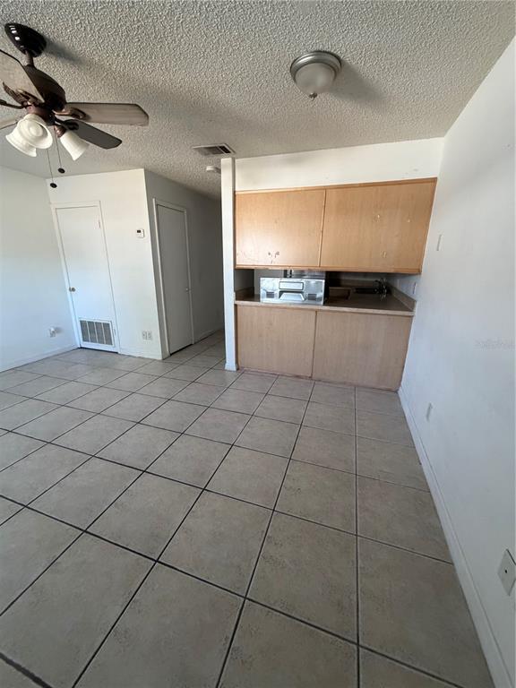A room with light-colored tile flooring, a ceiling fan, and wooden kitchen cabinetry — 6 LAKE VILLA WAY, KISSIMMEE, FL