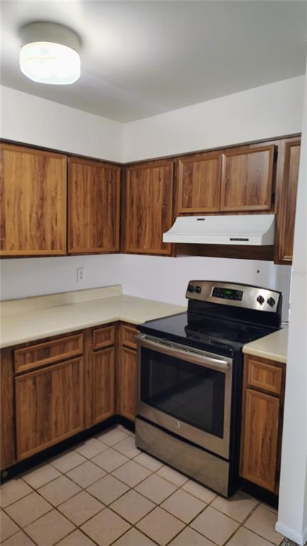 A kitchen features wood-grain cabinets, a stainless steel stove, and light-colored tile flooring — 6 LAKE VILLA WAY, KISSIMMEE, FL