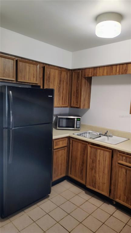A kitchen features wood-grain cabinets, a black refrigerator, a microwave, and a white sink — 6 LAKE VILLA WAY, KISSIMMEE, FL