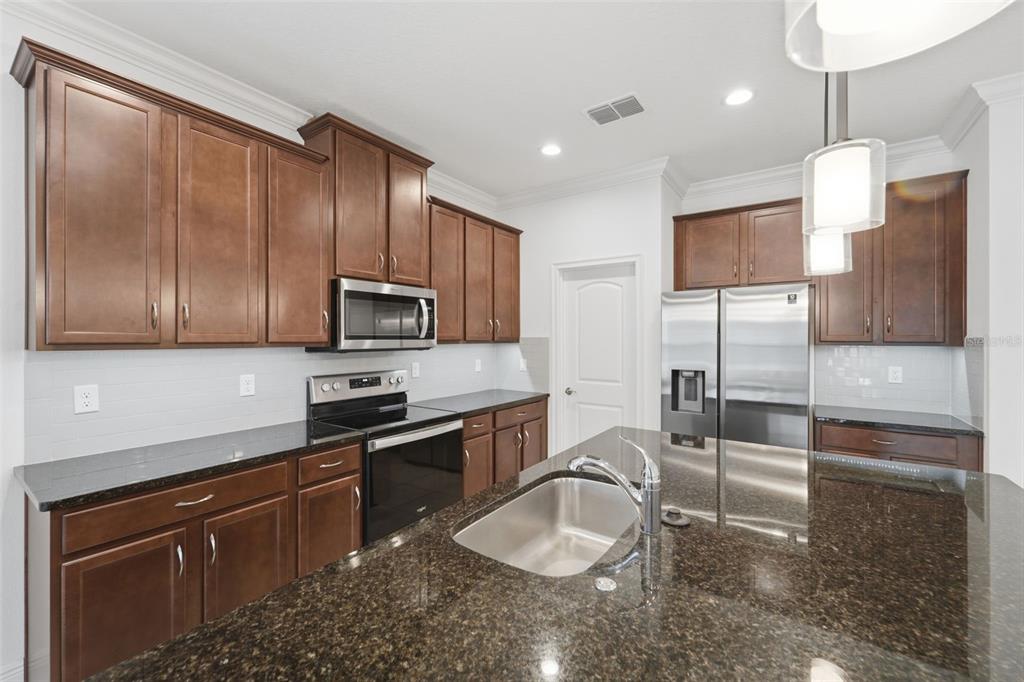 A kitchen with dark wood cabinets, granite countertops, stainless steel appliances, and a central island — 5576 ESTERO LOOP, PORT ORANGE, FL