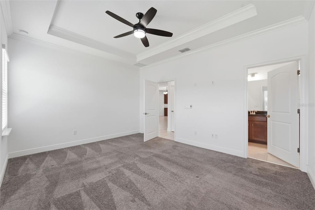 A bedroom with gray carpet, white walls, a tray ceiling, and an attached bathroom — 5576 ESTERO LOOP, PORT ORANGE, FL