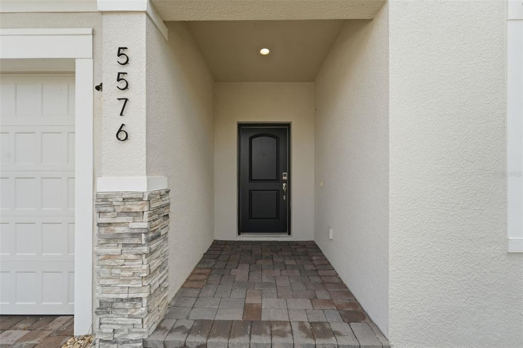 A covered entryway features a dark front door, stone accents, and a paver floor — 5576 ESTERO LOOP, PORT ORANGE, FL