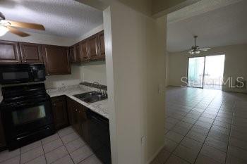 A kitchen with dark wood cabinets and black appliances opens into a tiled living area — 1155 THAYER STREET, SAFETY HARBOR, FL