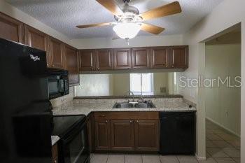 A kitchen features wood cabinets, granite countertops, a ceiling fan, and black appliances — 1155 THAYER STREET, SAFETY HARBOR, FL
