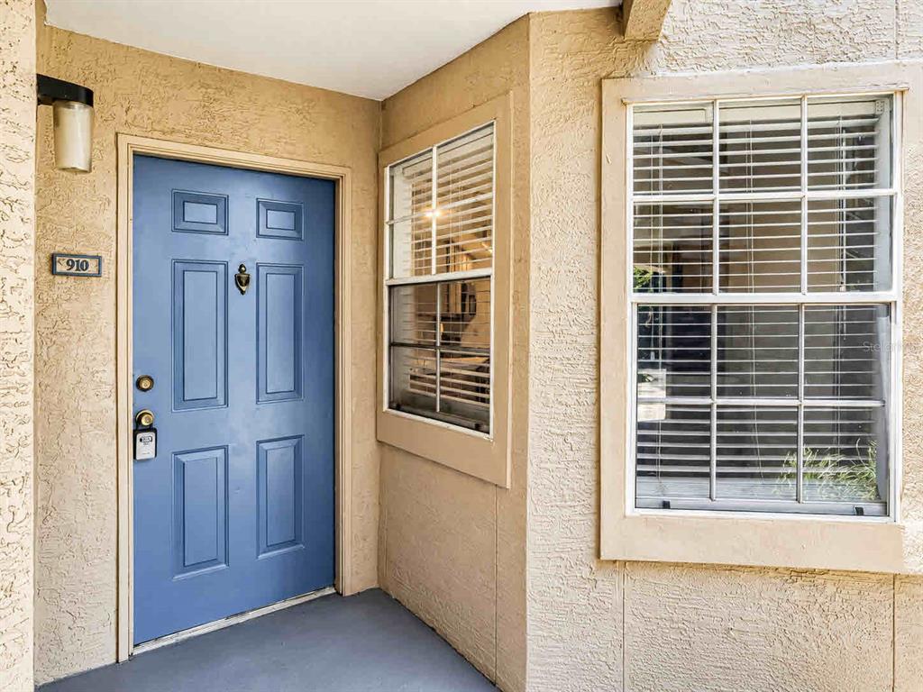 A blue front door with a number plate and a window with blinds on a stucco exterior — 7270 WESTPOINTE BOULEVARD UNIT 910, ORLANDO, FL