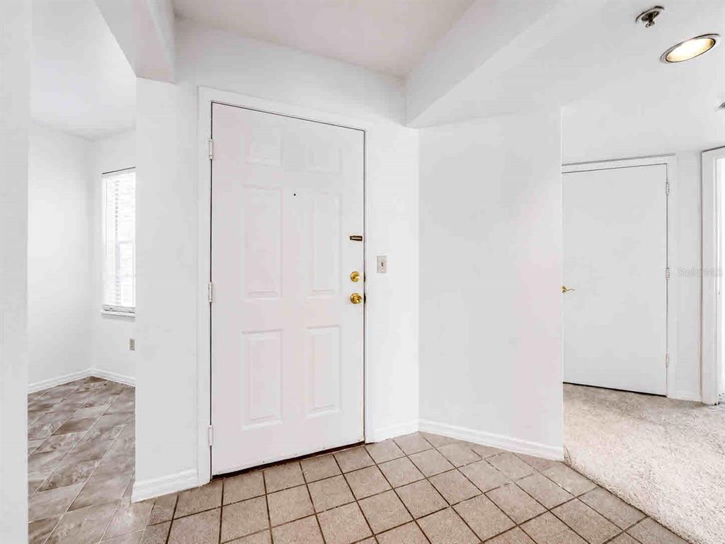 An entryway with a white front door, tiled floor, and adjacent carpeted room — 7270 WESTPOINTE BOULEVARD UNIT 910, ORLANDO, FL