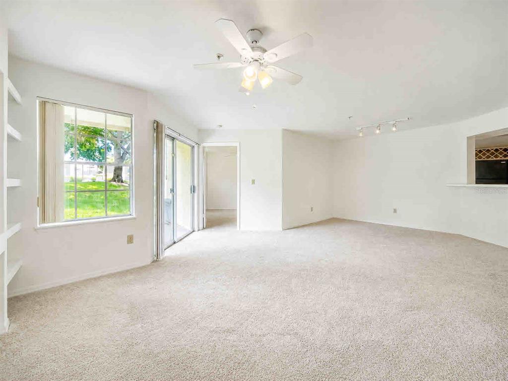 An empty living room features beige carpeting, a ceiling fan, and a sliding glass door — 7270 WESTPOINTE BOULEVARD UNIT 910, ORLANDO, FL