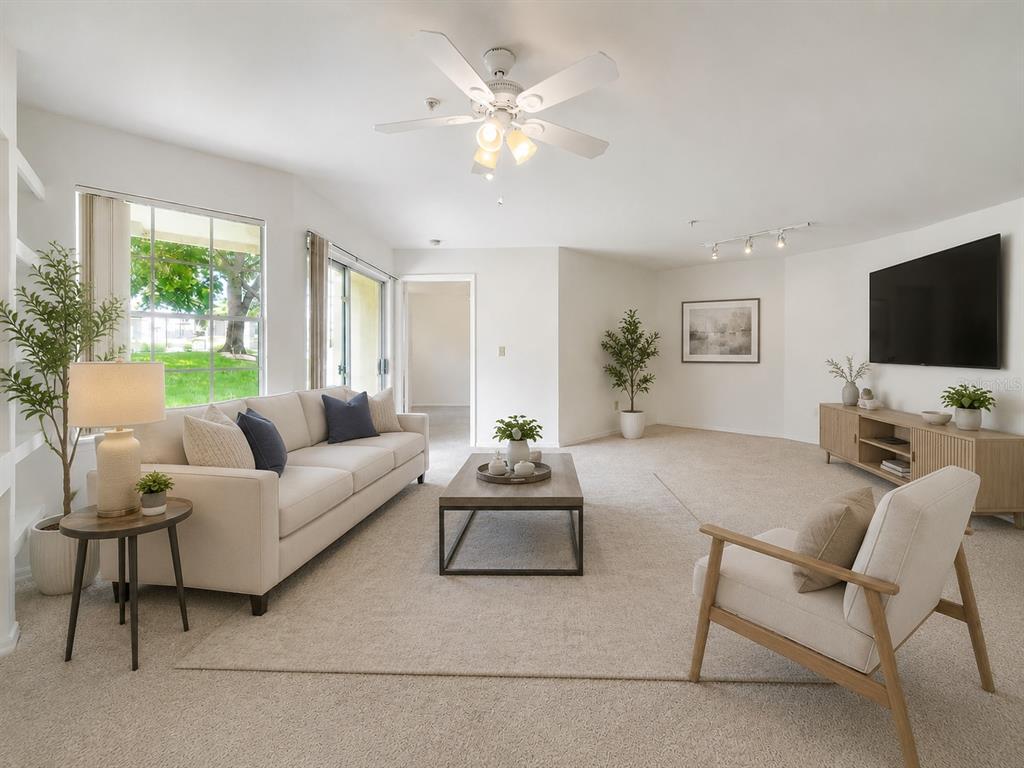 A bright living room features a beige sofa, armchair, coffee table, and a wall-mounted television — 7270 WESTPOINTE BOULEVARD UNIT 910, ORLANDO, FL
